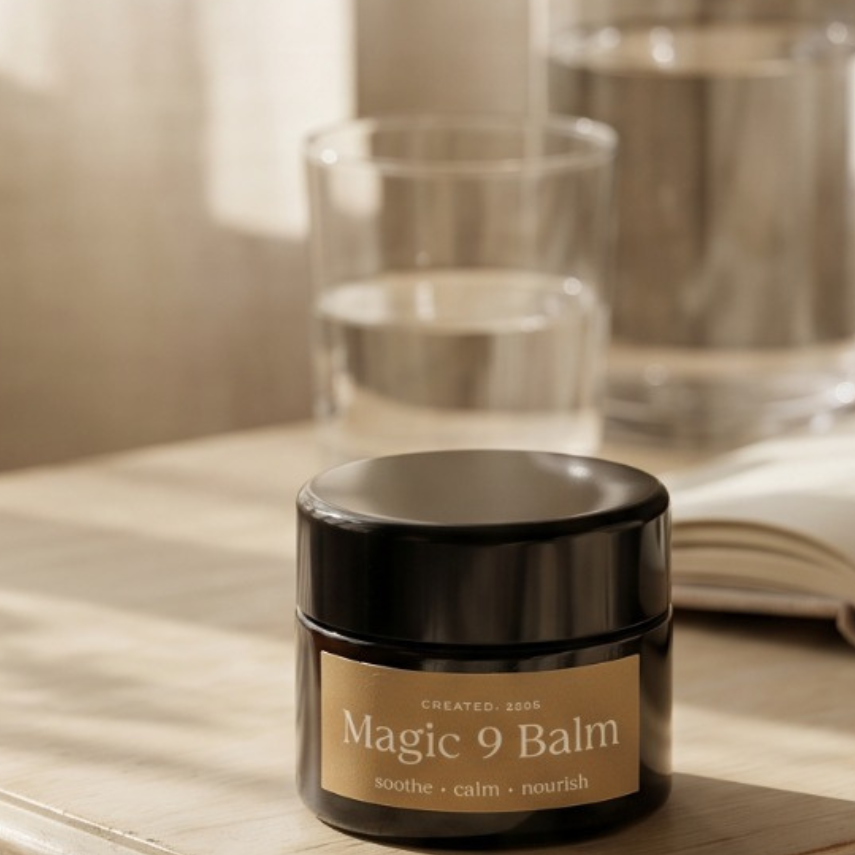 Jar of 'Magic 9 Balm' on a wooden surface with a book and glass in the background